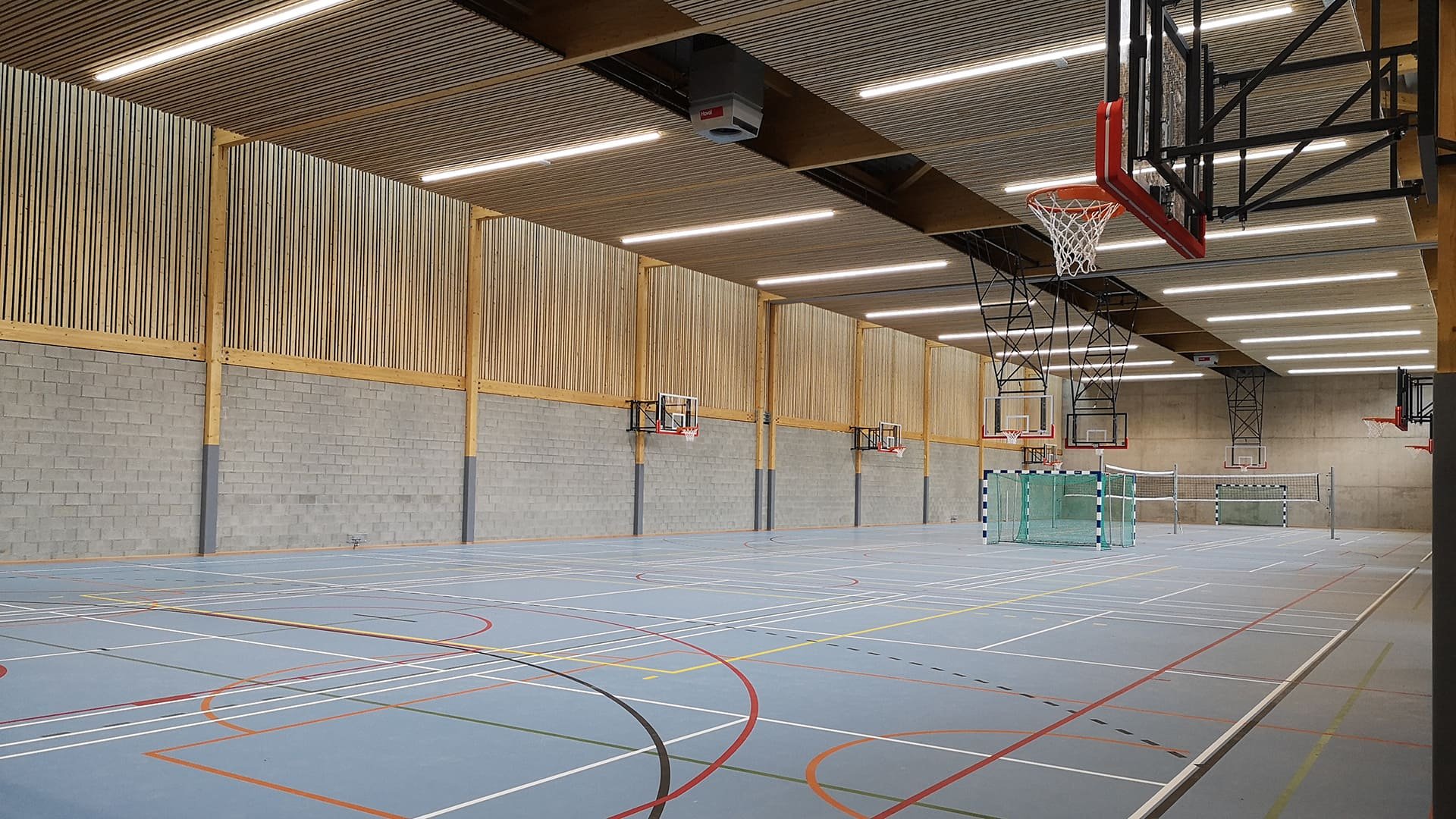 Intérieur de la salle de sport de l'école de L'Inda: on y voit un grand terrain de basket où il y a été déposé 2 goals de foots, 2 filets de volley. L'intérieur est très moderne en bois et beton